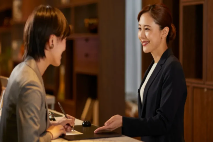Mulher sorrindo enquanto hóspede preenche ficha na gestão de equipe hotel