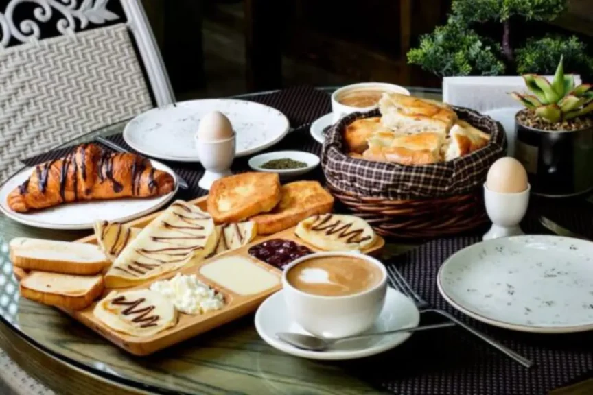 Mesa com café da manhã de hotel servido com pães, frutas, ovos e bebidas